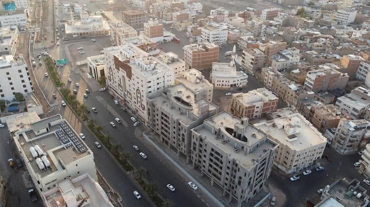 Existing urban aerial photograph showing a curving road and dense flat-roofed buildings in the Madinah district.