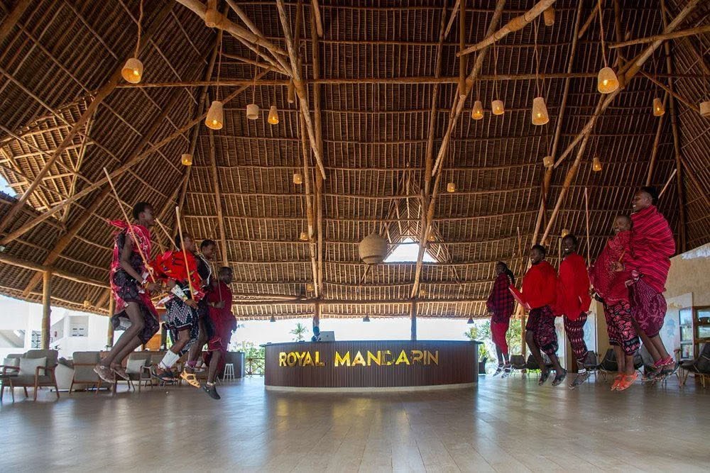 Royal Mandarin site photograph of performers in red clothing jumping beneath a high timber and thatch roof near the reception desk.