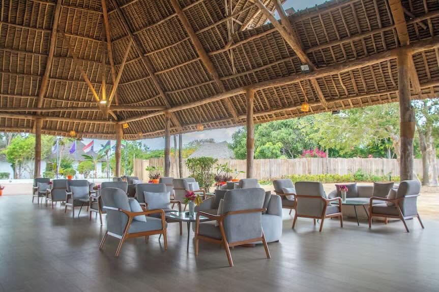 Royal Mandrine Resort site photograph of an open lounge under a high timber and thatch roof, with upholstered chairs and tables.