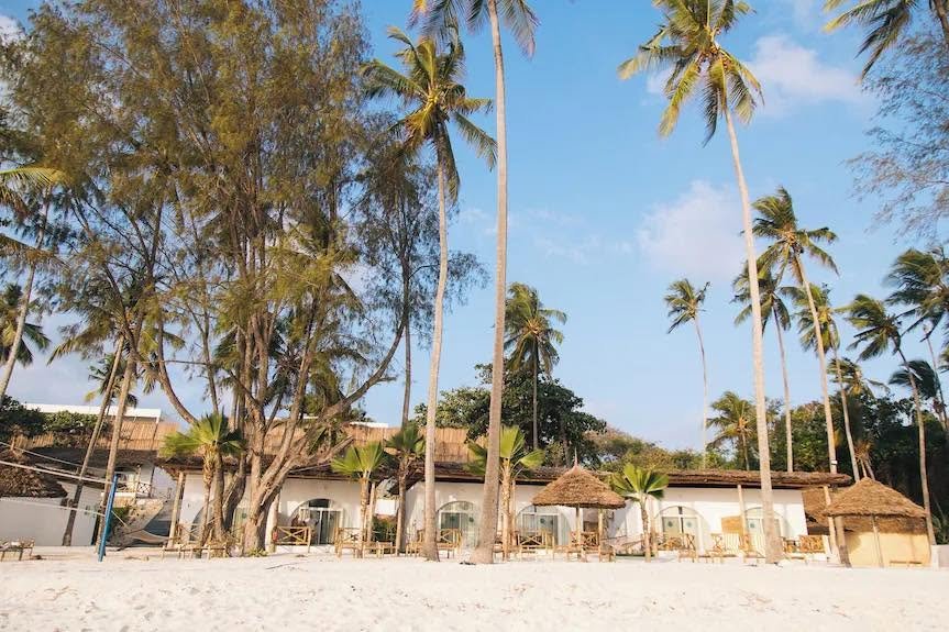 Royal Mandrine Resort site photograph of a long row of white arched rooms behind tall palms and sandy beachfront.