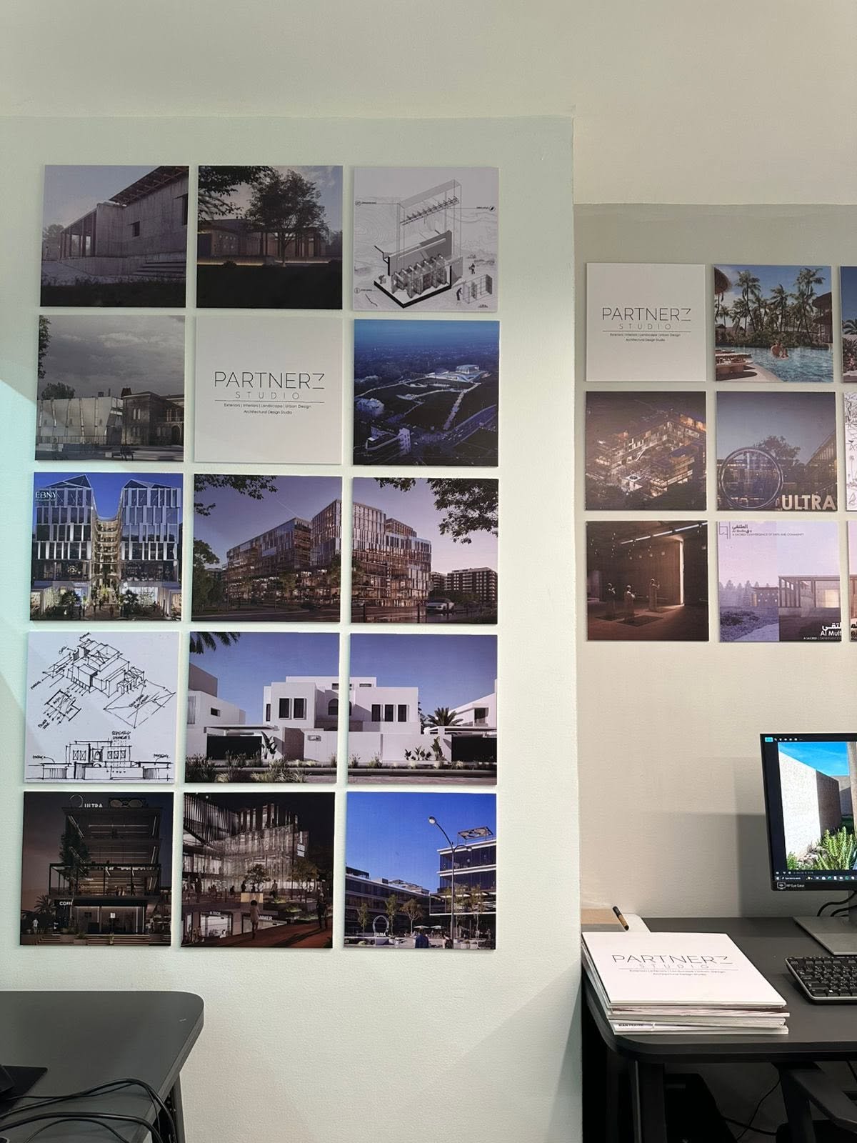 Office display of architectural drawings and renderings above a desk with a monitor and Partnerz presentation booklets.